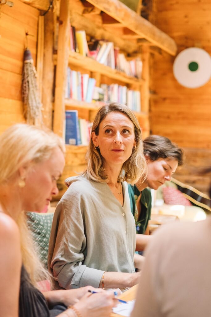 Group of adults engaged in discussion in a warm, cozy wooden interior with bookshelves.