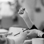 Black and white image of people collaborating at a desk, focusing on hands writing.